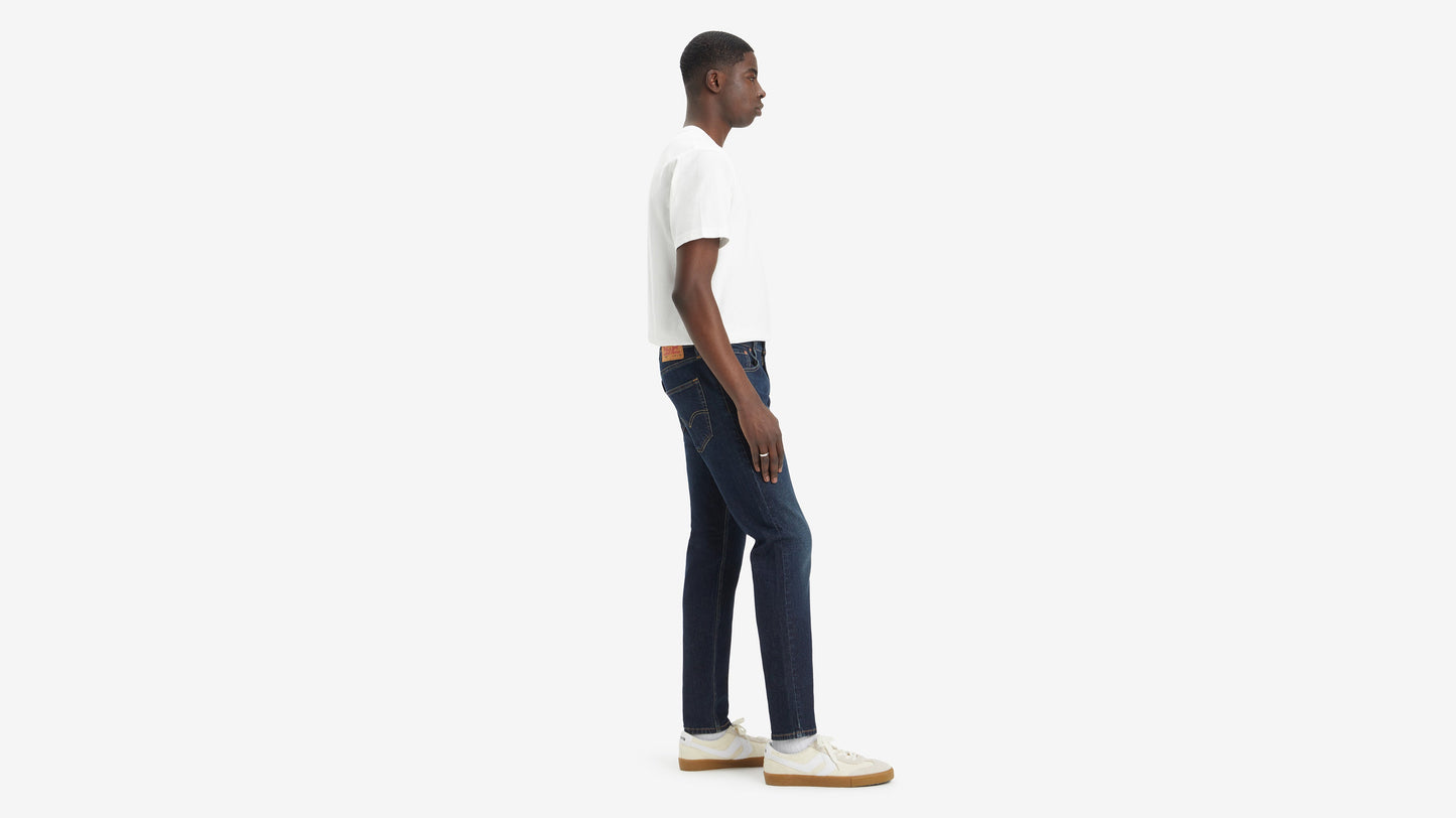 Side view of model in Levi’s 512 jeans, paired with white tee, & sneakers