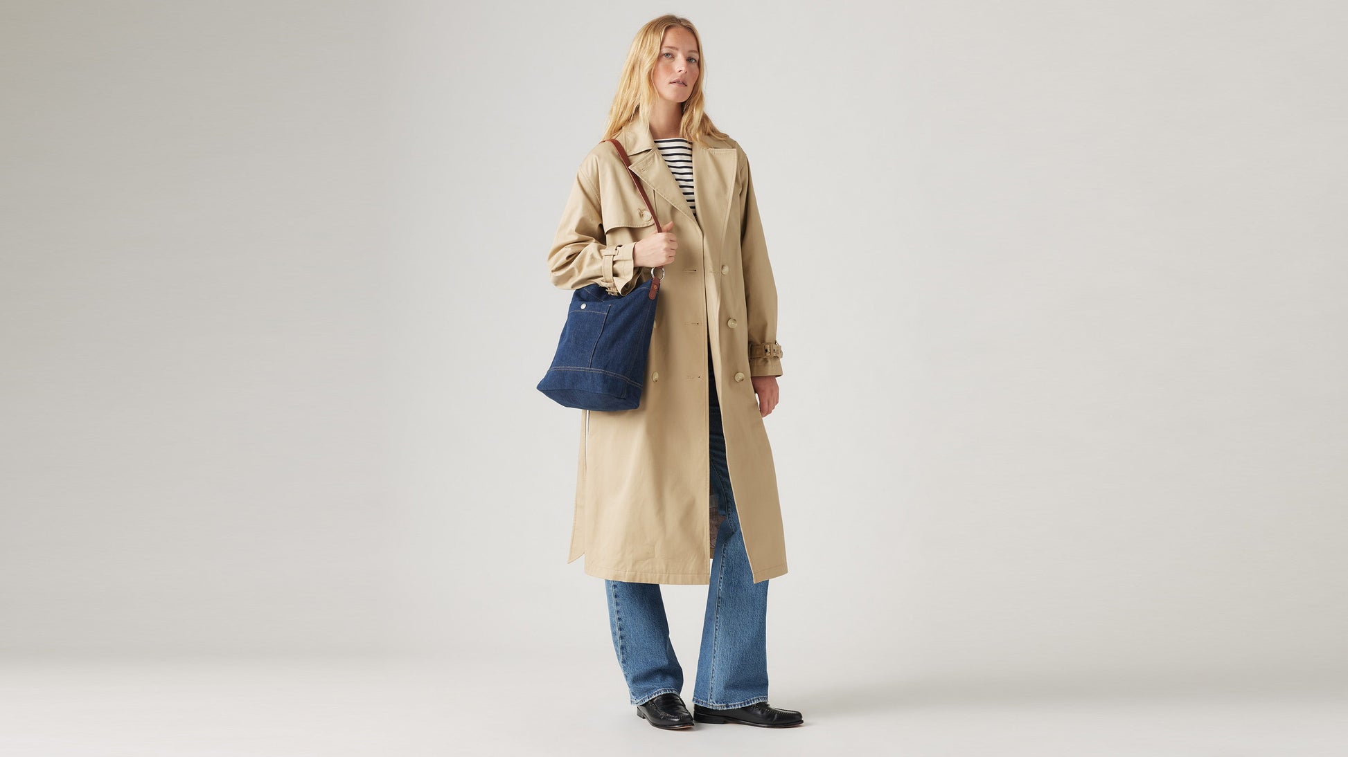 Full-length view of a model in a beige trench coat and striped shirt