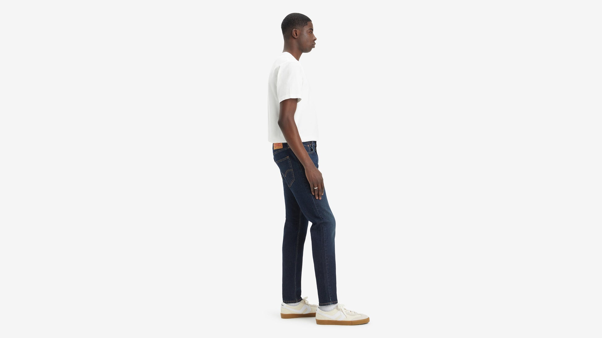 Side view of model in Levi’s 512 jeans, paired with white tee, & sneakers